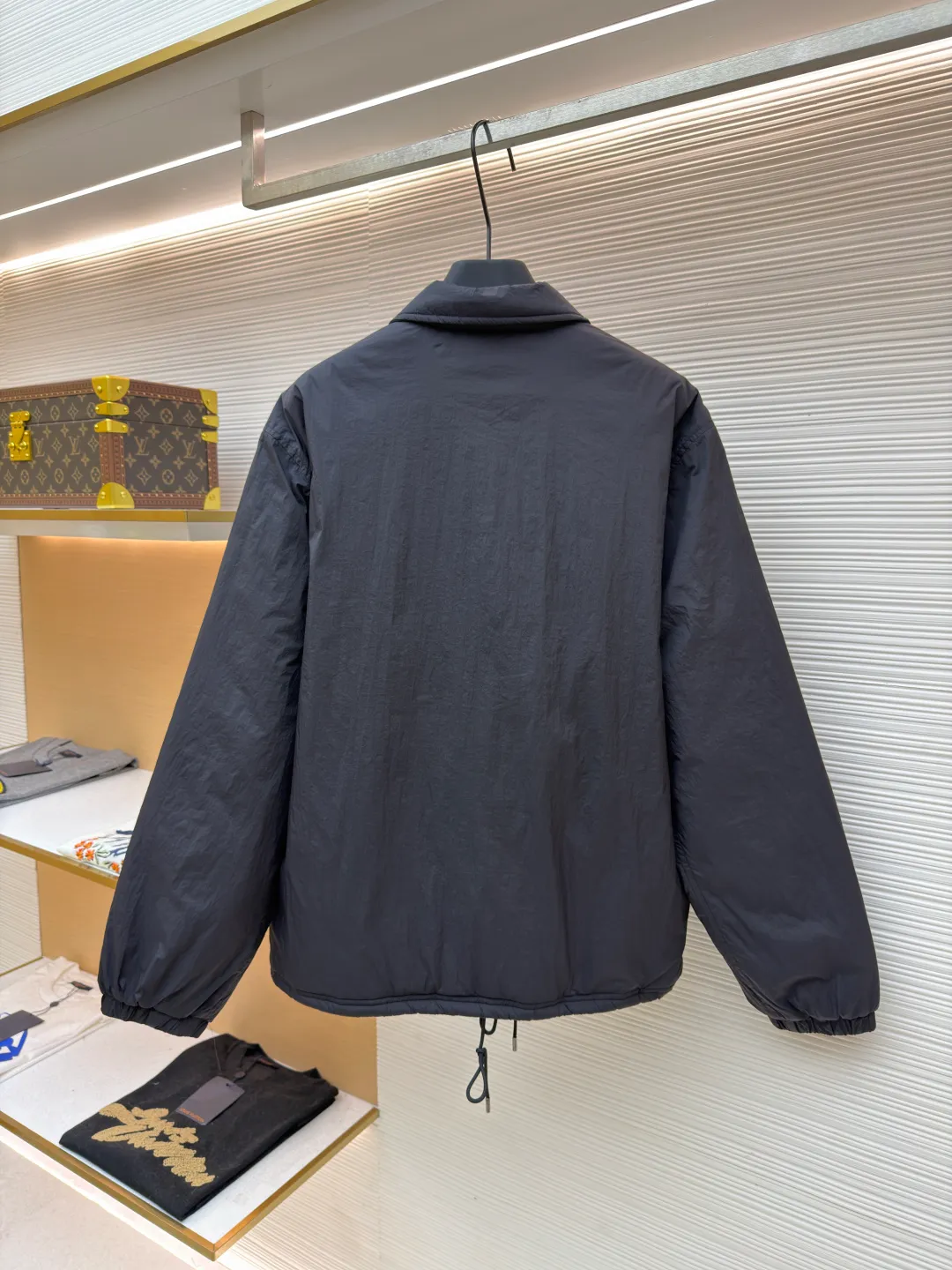 Ralph Lauren red label light cotton jacket (coach jacket) ●Original version: purchased and developed for 2699 ●Item number: 1681910-B90 ●Fabric: high-density nylon taffeta fabric ●Technology: embroidery production ●Color: black ●Version: fitted version ●Weight: about 340 grams ●Size: S-M-L-XL ●Description: The density of high-density nylon taffeta is about 210T-300T, with a smooth and slightly matte surface, excellent windproof and waterproof properties (with DWR water-repellent treatment), strong wrinkle resistance and easy care, in line with the positioning of American casual "durable and practical". Classic dark black, using vat dyeing process (dye penetrates into the fiber), the color fastness reaches ISO level 4 or above, preventing fading or color transfer after washing. The lightweight cotton-polyester blend lining (65% Polyester + 35% Cotton) reduces the friction between the fabric and inner clothing, improving the smoothness of wearing; the blended material combines breathability and durability to avoid the stuffy feeling of pure nylon lining. The classic Coach Jacket has a loose fit with slightly dropped shoulder lines (shoulder width is 1-2cm wider than the standard fit). The length reaches the hips and the sleeves are slightly tapered straight sleeves, taking into account both freedom of movement and casual style. Polo horse logo on the left chest: flat satin stitch embroidery (satin embroidery), embroidery thread: 100% polyester high color fastness embroidery thread (the color number is consistent with the brand's standard red color card), stitch density 12-15 stitches/cm, the outline of the horse logo is clear, and the details of the rider and horse are burr-free. Embroidery positioning: precise positioning through the template (12cm from the neckline and 8cm from the placket) to ensure left and right symmetry and centering. Topstitching technology: The seams of the body are made of double-needle flat seams (needle pitch 3cm/10 needles), the stitches are smooth and straight, the stitching color is dark black (the same color as the fabric), and the stitch width is 0.5cm, which enhances firmness while forming simple decorative lines. The splicing of the front placket and the body: the placket is made of double-layer folding + flat seam splicing, with a thickness of about 0.3cm to ensure that the buttons are not easily deformed when fixed; the edges of the placket are cut with a hot knife to avoid burrs. The sleeves are spliced ​​to the body: the armholes are spliced ​​with round-head keyhole machine seams + flat seams. After splicing, the armholes have a natural curvature and no sense of tightness during movement; the height of the sleeves is about 8-10cm, which is in line with the loose characteristics of casual jackets. Main button: black urea resin button, matte surface treatment, buttonholes are hand-made keyholes (6 strands of cotton thread, keyhole density 8 stitches/mm), and the edges of the eyelets are smooth and without burrs. Collar buttons: The first button on the collar is a hidden button (diameter 12mm), which prevents the collar from opening and improves the neatness of wearing.